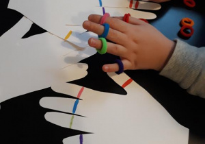 Zdjęcie przedstawia chłopca nakładającego na palce kolorowe gumki do włosów według wzoru.